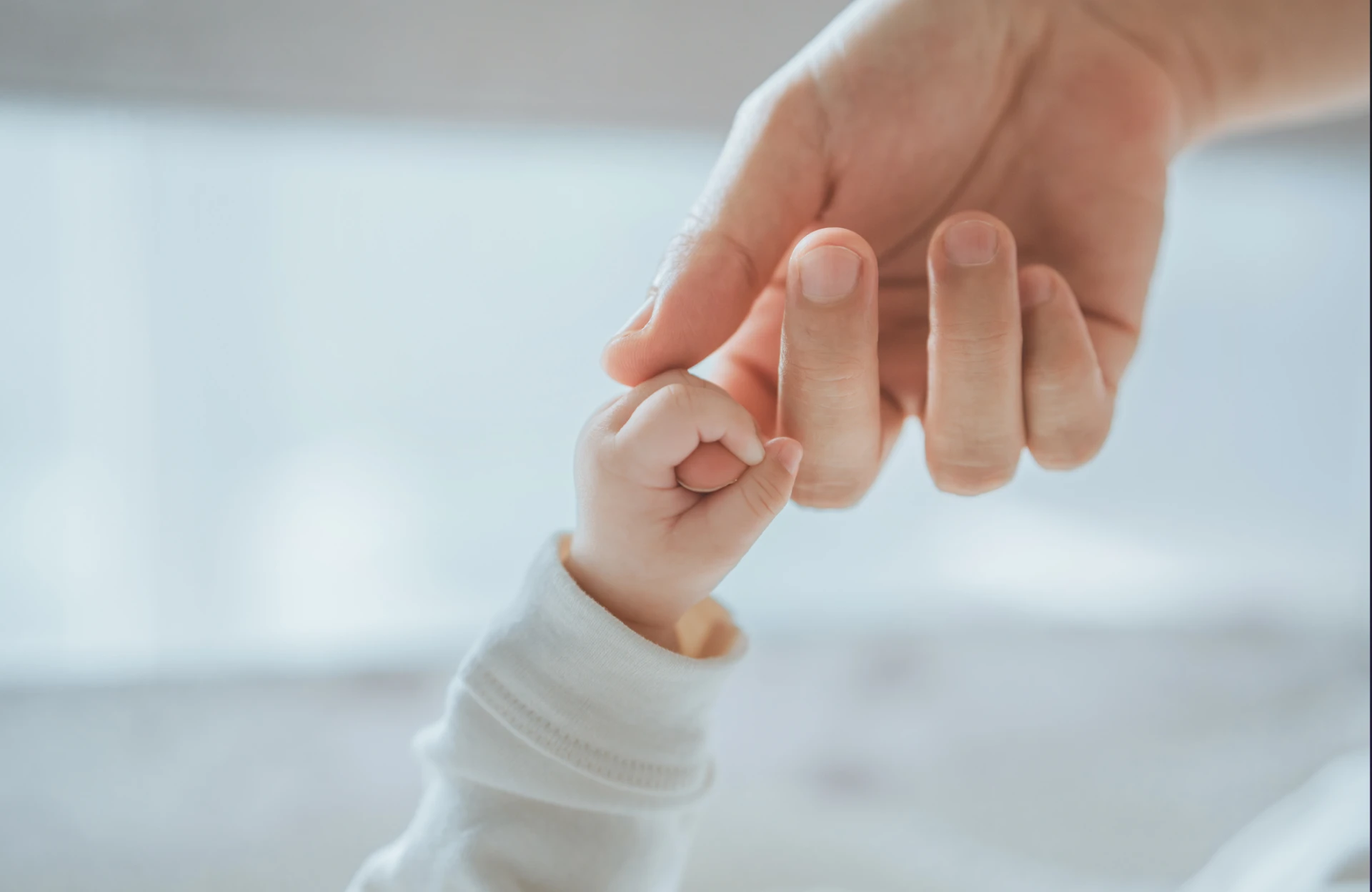 A newborn's hand holding an adult's finger
